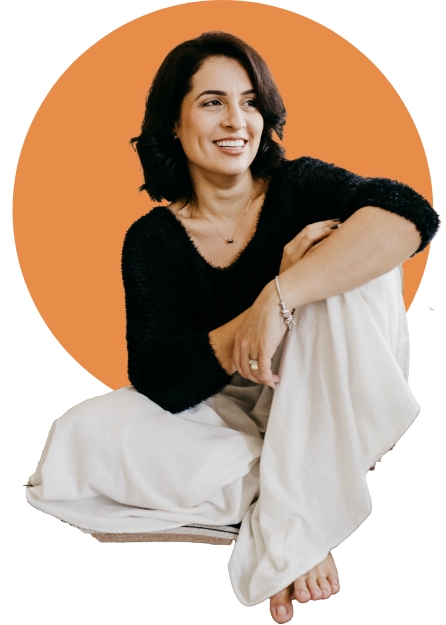 Woman sitting leaning on left leg, smiling, with orange circle behind her